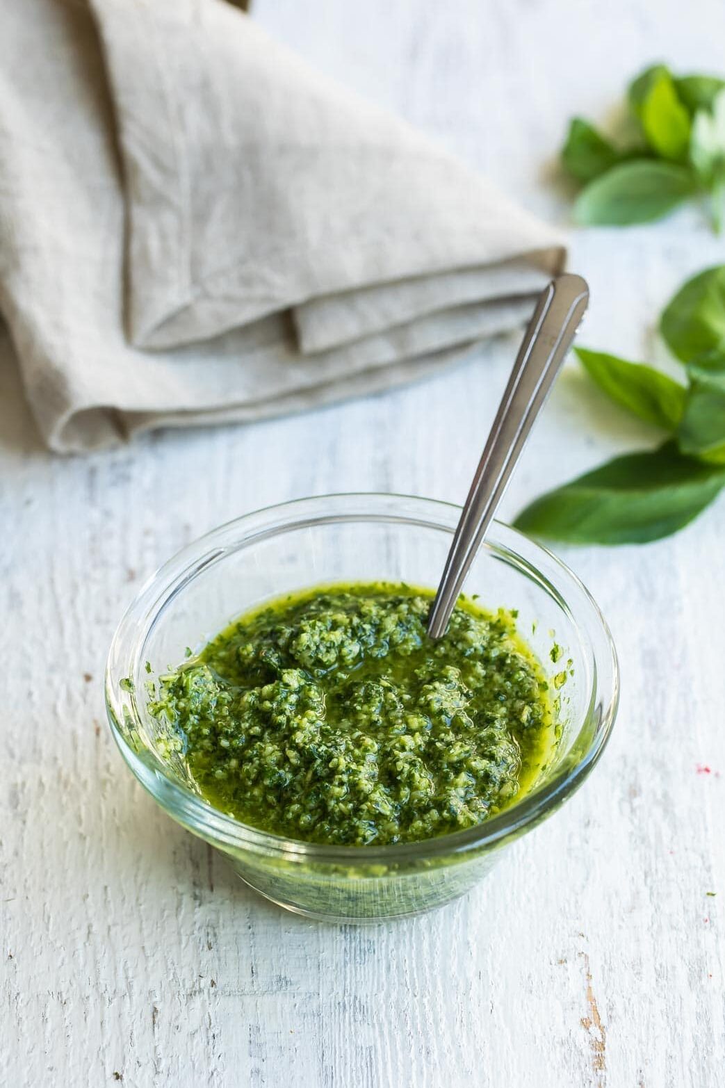 Basil pesto in a clear bowl with a spoon.