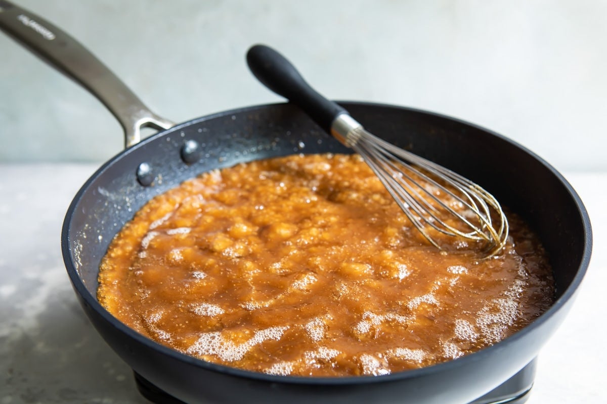 Butter and brown sugar combined in a black pan with a whisk.