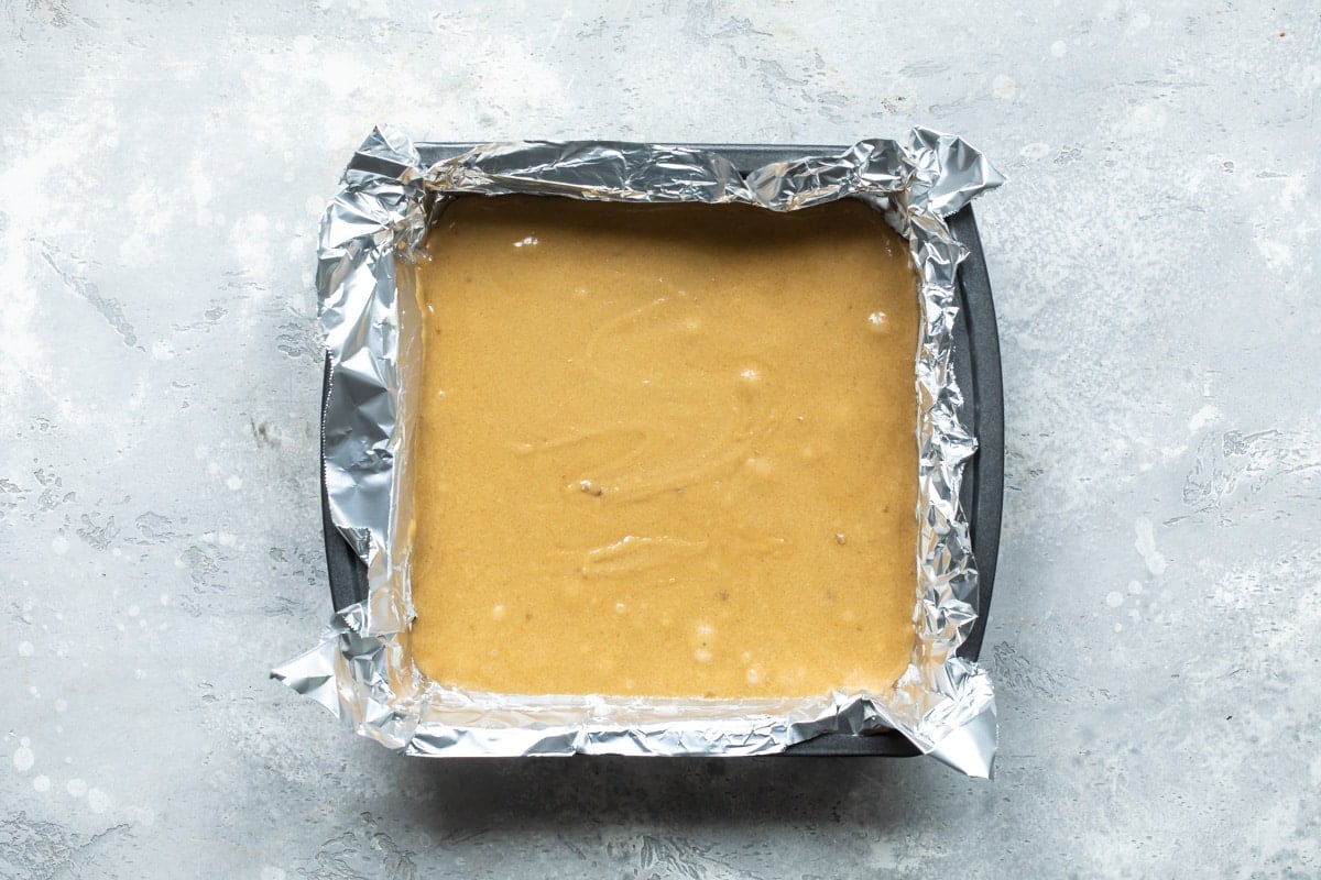 Blondie batter in a square baking pan lined with tin foil.