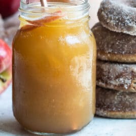 Brandy apple cider slush in a mason jar next to a stack of four brown donuts.