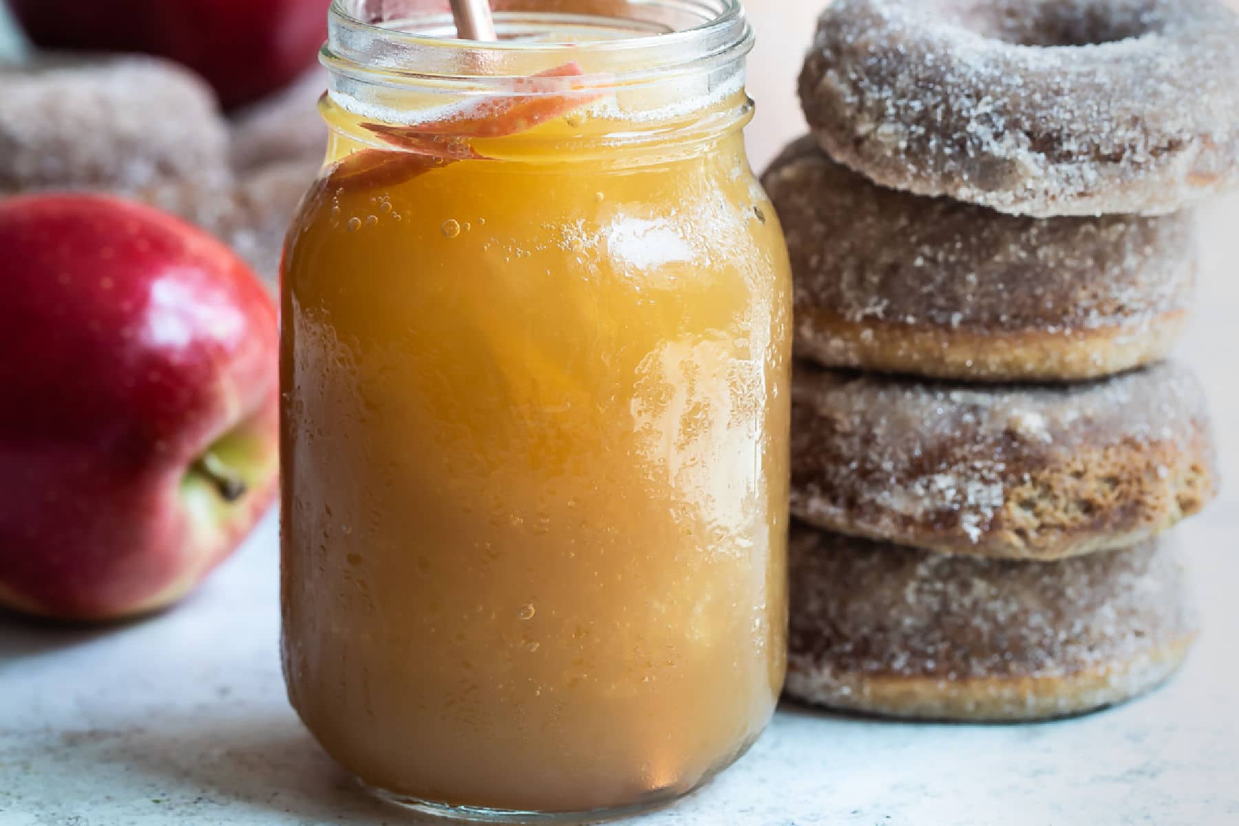 Brandy apple cider slush in a mason jar next to a stack of four brown donuts.