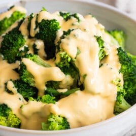A bowl of blanched broccoli with cheese sauce drizzled on top.