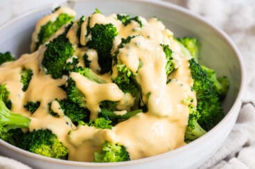 A bowl of blanched broccoli with cheese sauce drizzled on top.
