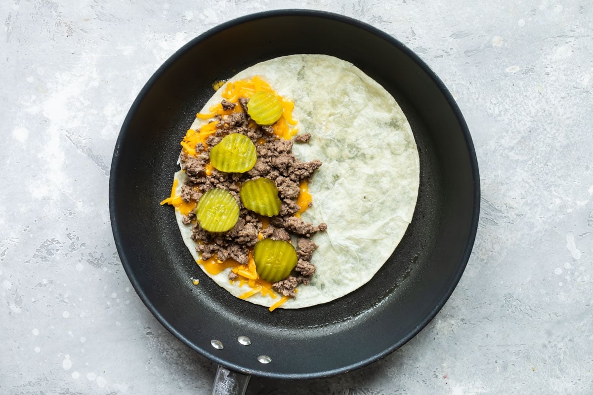 An open-faced cheeseburger quesadilla in a skillet.