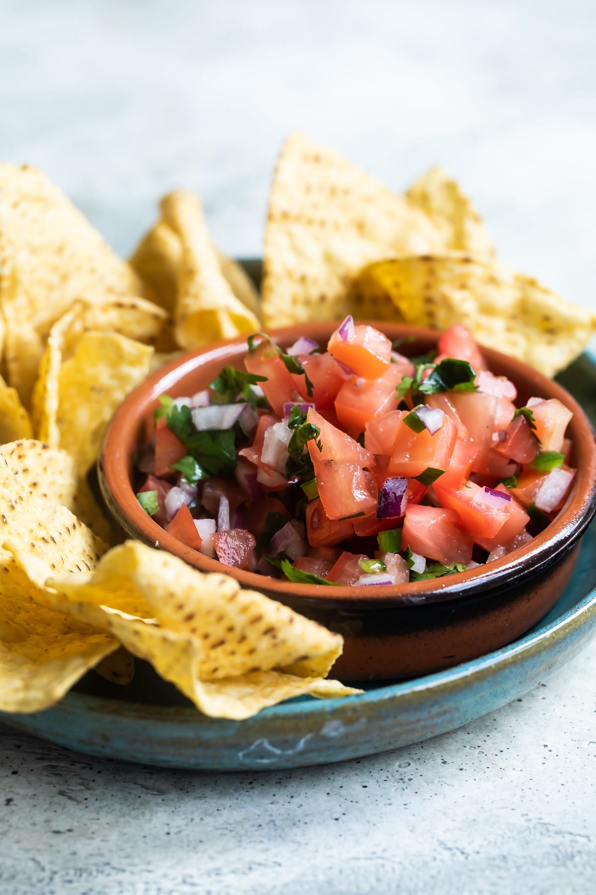 Chipotle tomato salsa in a red bowl on a blue plate with tortilla chips.