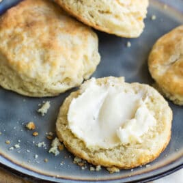 A plate with biscuits cut in half, one piece slathered in butter.