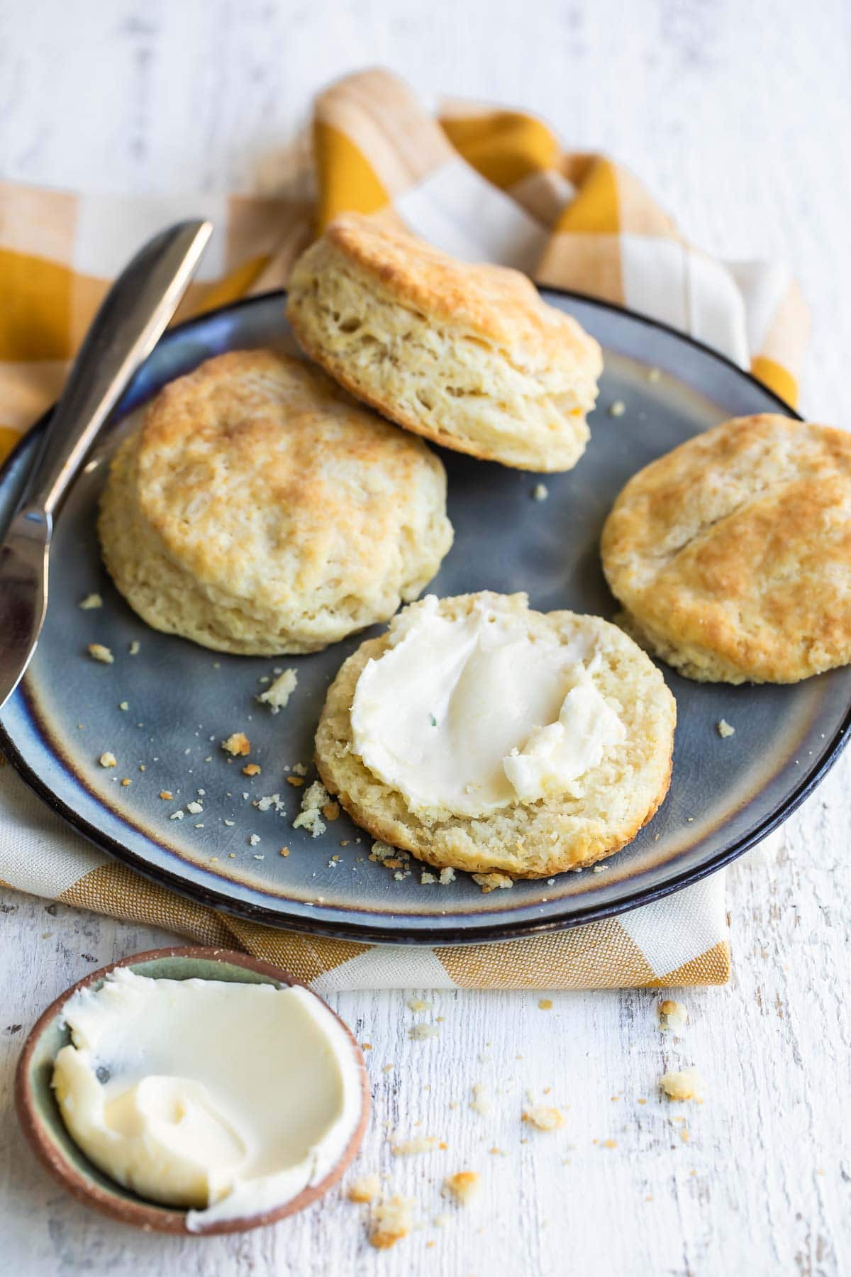 A plate with biscuits cut in half, one piece slathered in butter.