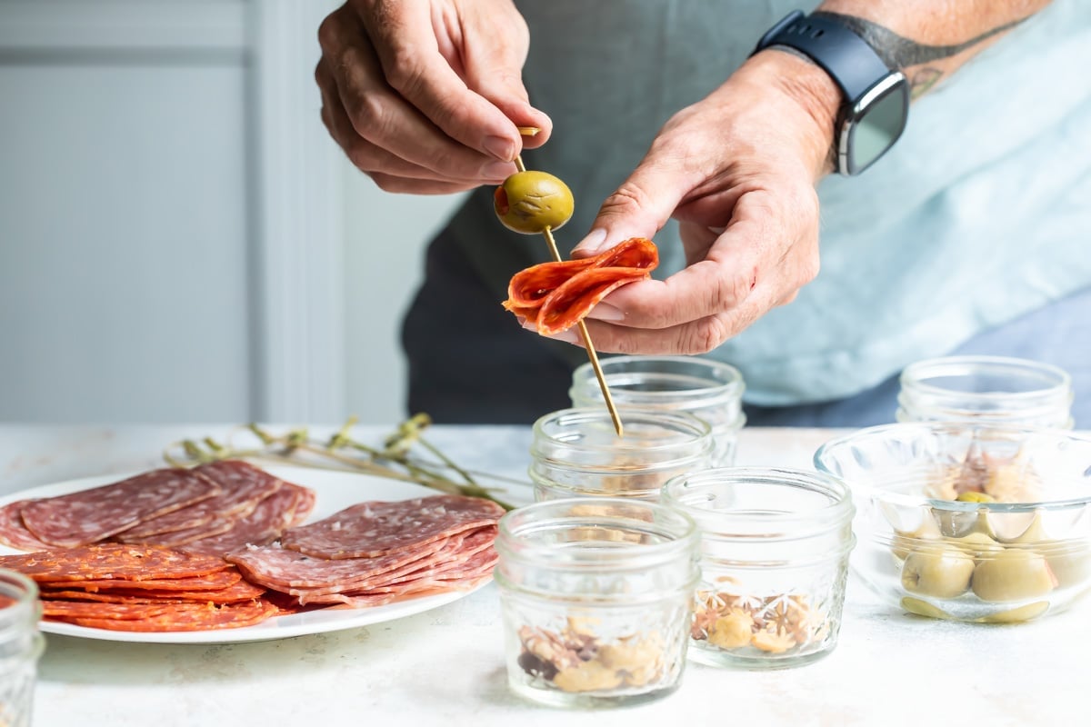 Someone poking a skewer with an olive through a folded piece of pepperoni.