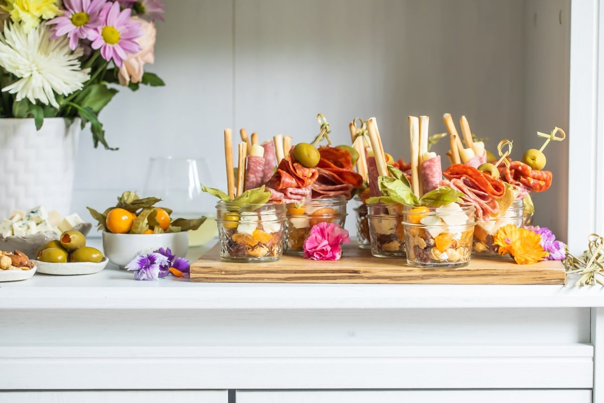 Jarcuteries on a wooden cutting board next to a vase of flowers.