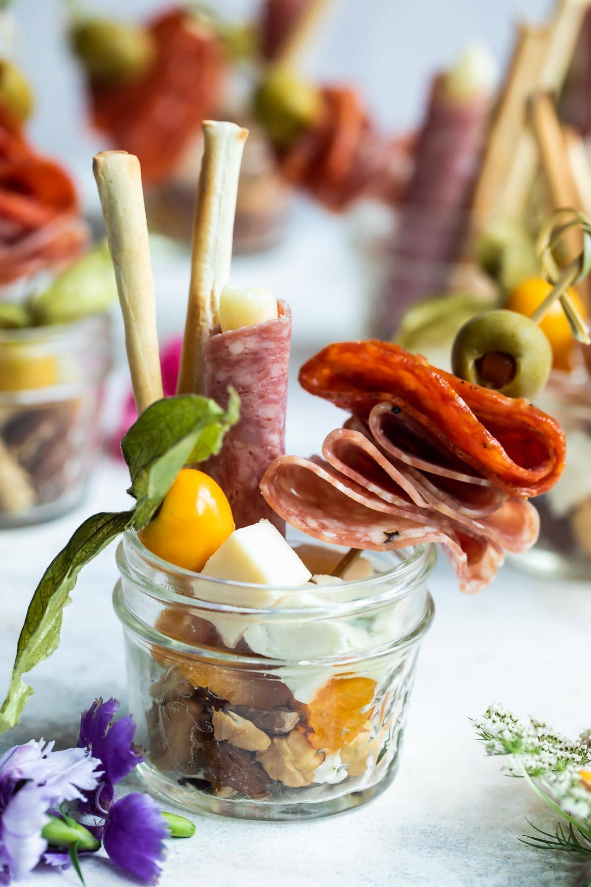 A mason jar filled with meats, olives, nuts, and breadsticks.