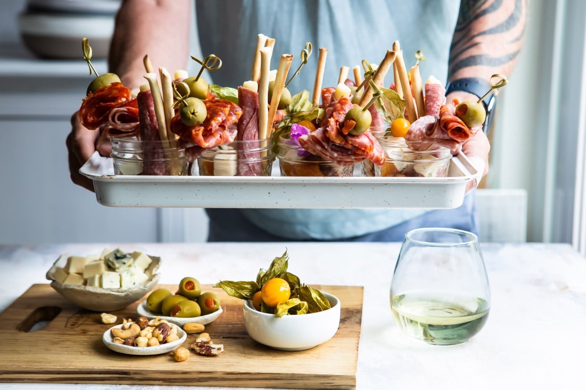Someone holding a white tray filled with jarcuterie.