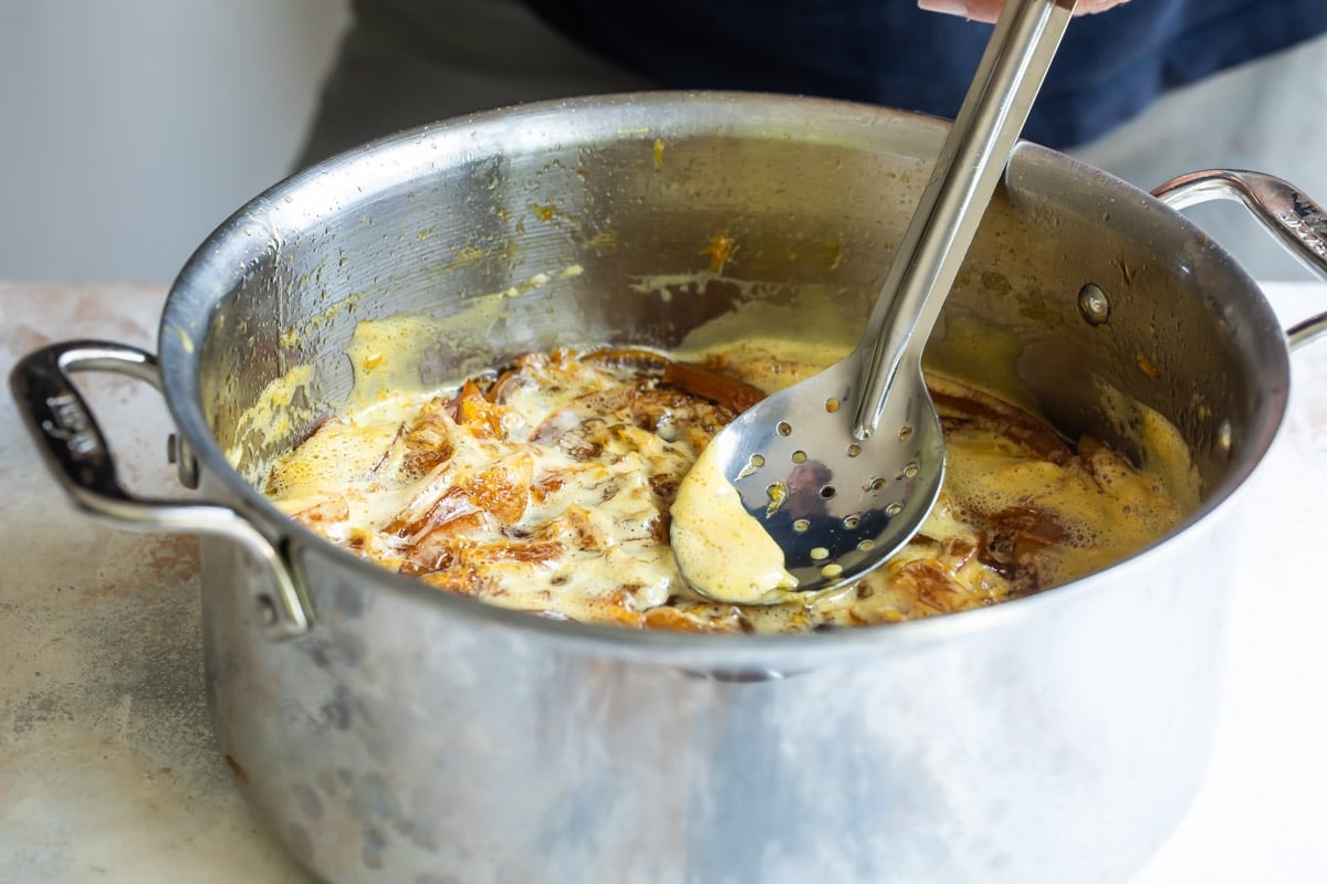 Scraping the foam off a pot of orange marmalade that is cooking.