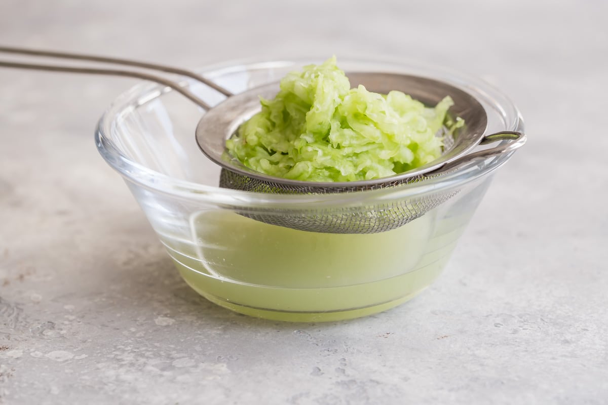 A side shot of chopped cucumber in a silver strainer.