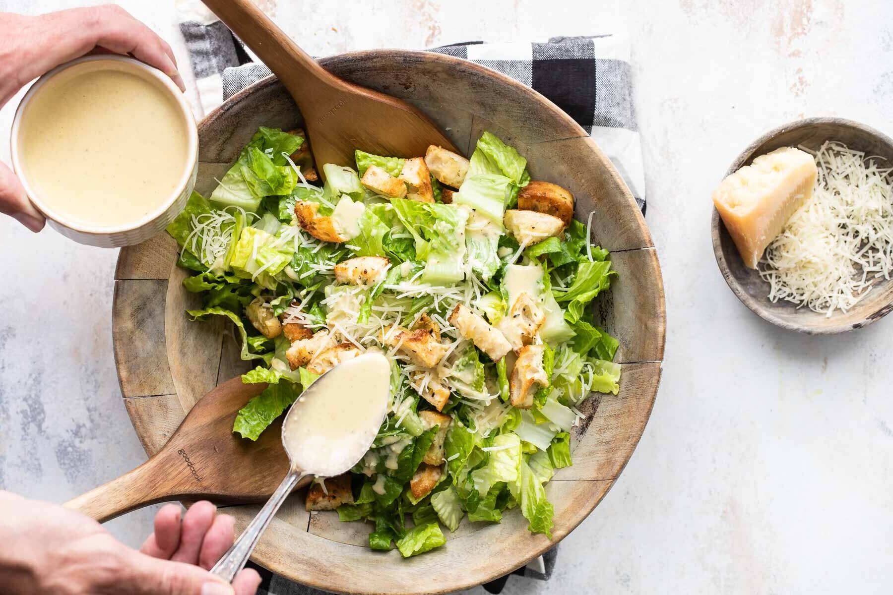 Someone spooning Caesar dressing on a Caesar salad.