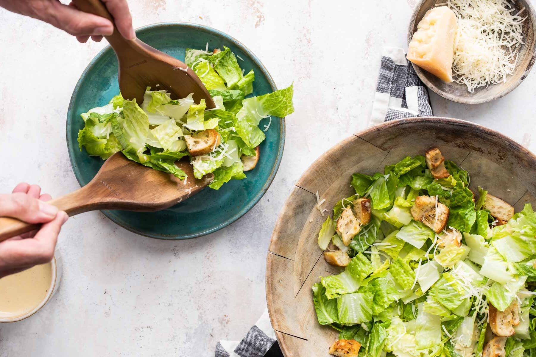 Caesar salad being put on a blue plate.