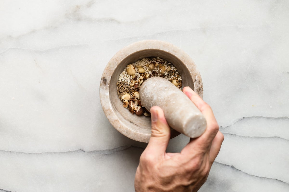 A hand crushing dukkah ingredients in a mortar and pestle.