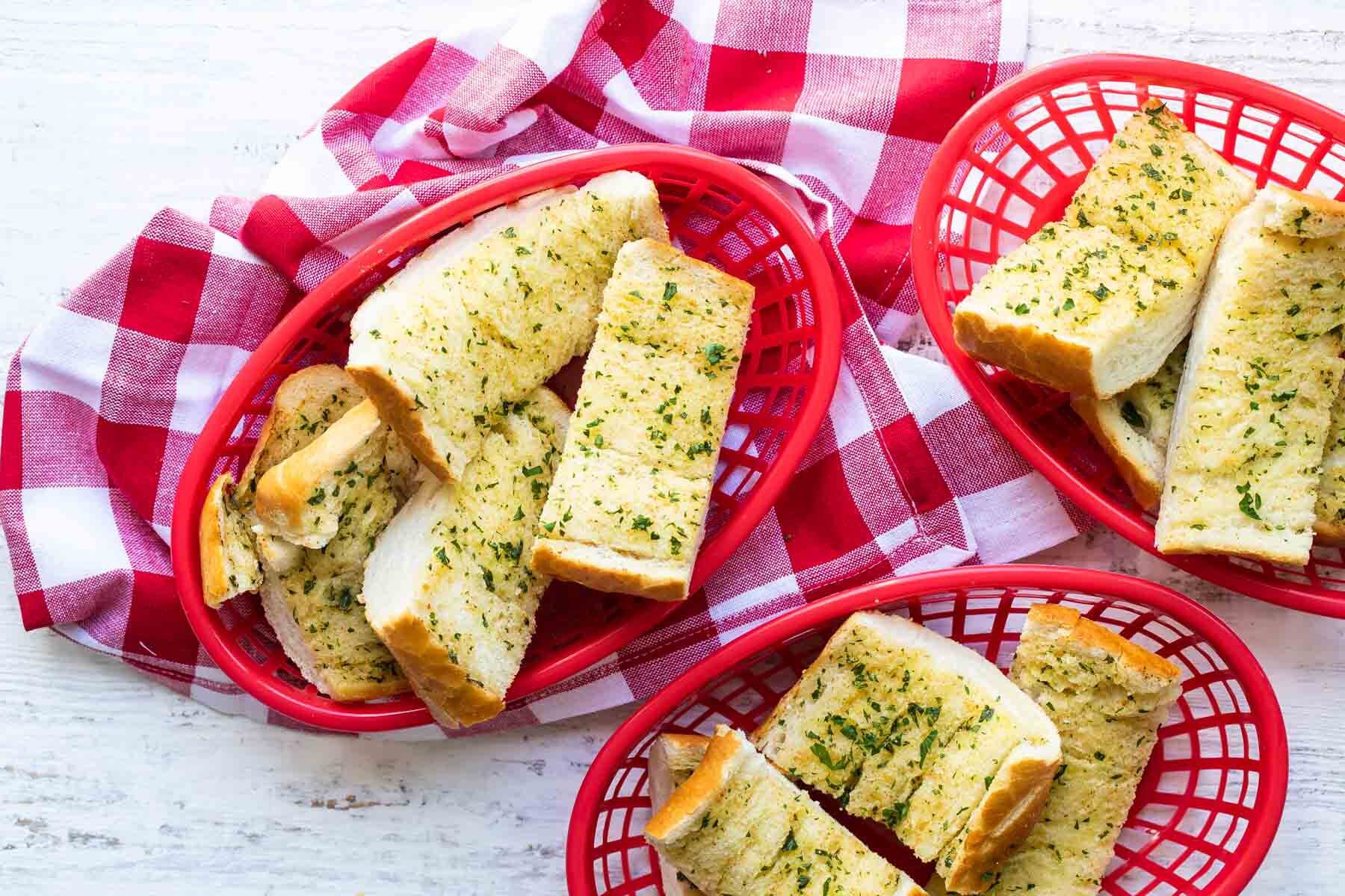 Garlic bread in three plastic red baskets.