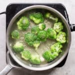 Broccoli cooking in boiling water in a silver pot.
