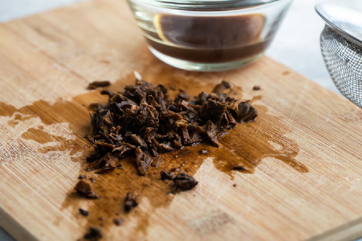 Dried mushrooms that have been rehydrated, minced on a cutting board.