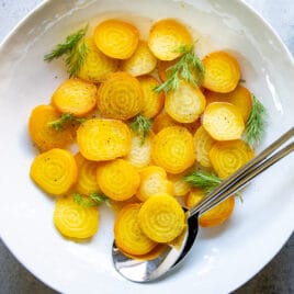 A platter of roasted golden beets, sliced and dressed with vinaigrette and fresh dill fronds.
