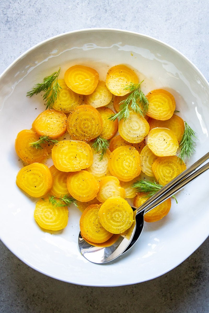 A platter of roasted golden beets, sliced and dressed with vinaigrette and fresh dill fronds.