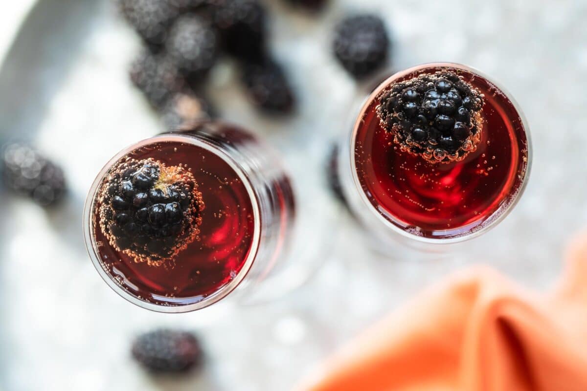 Two Kir Royale cocktails in champagne flutes on a metal tray.