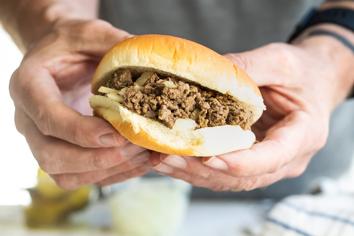 Two hands holding a loose meat sandwich.