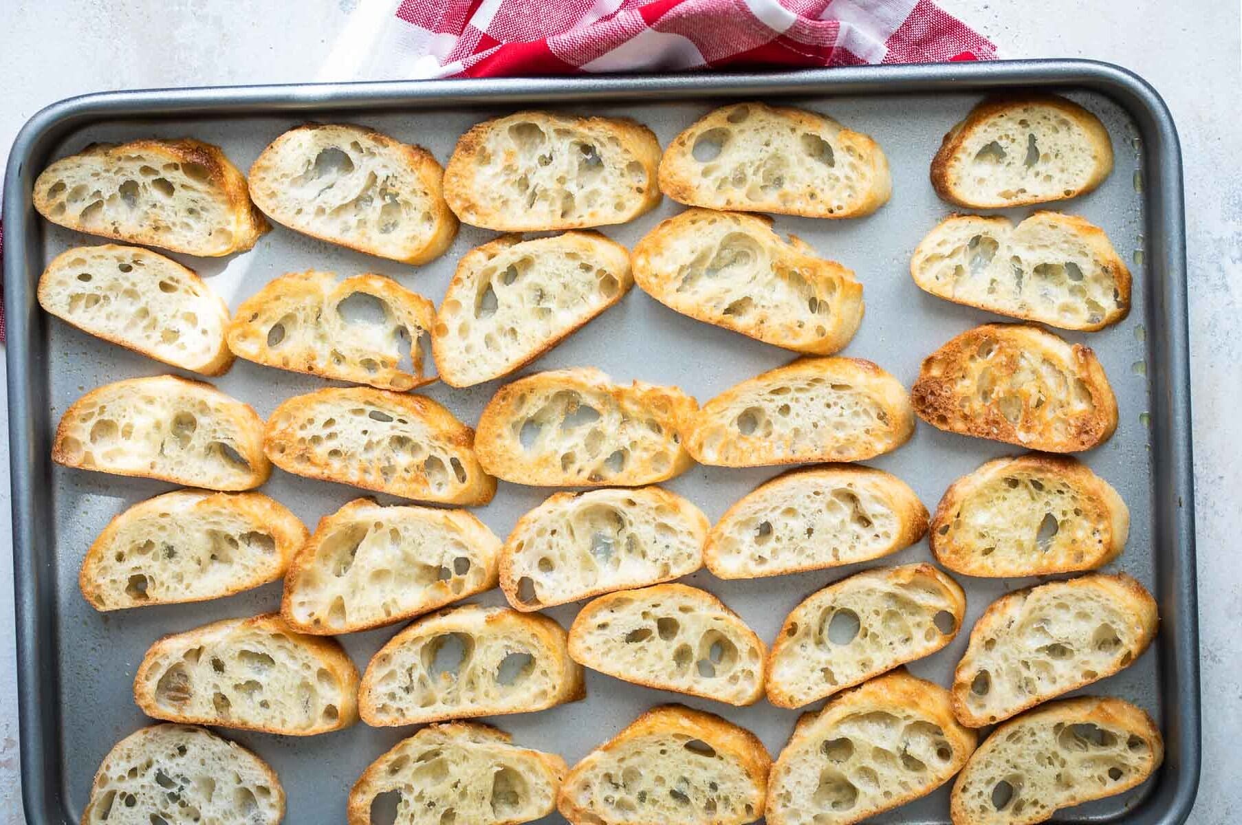 Toasted baguettes on a baking sheet.