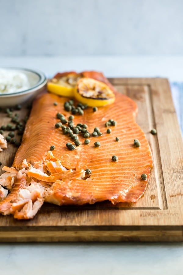Smoked salmon on a wooden board with capers and lemon slices on top.