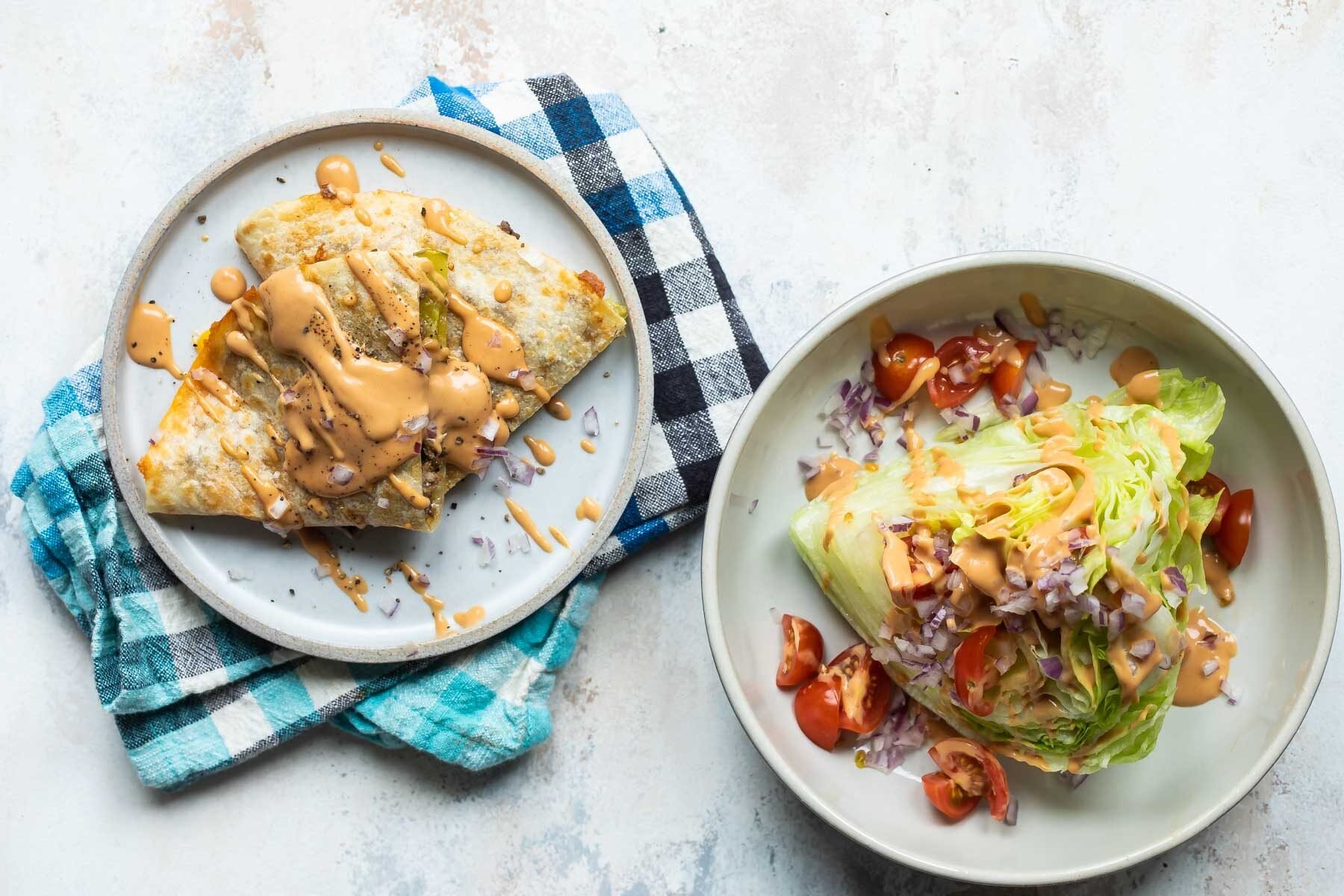 A cheeseburger quesadilla stacked on a plate next to a wedge salad.