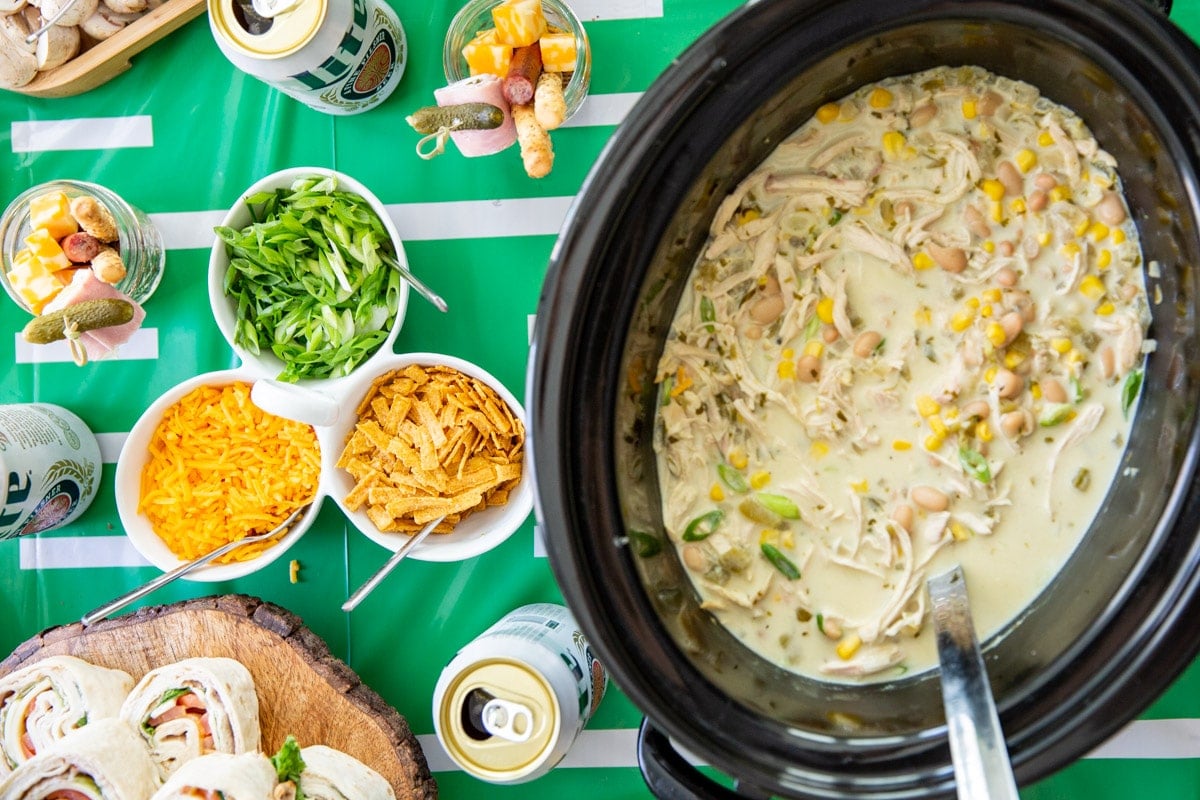 White chicken chili in a slow cooker with toppings nearby.
