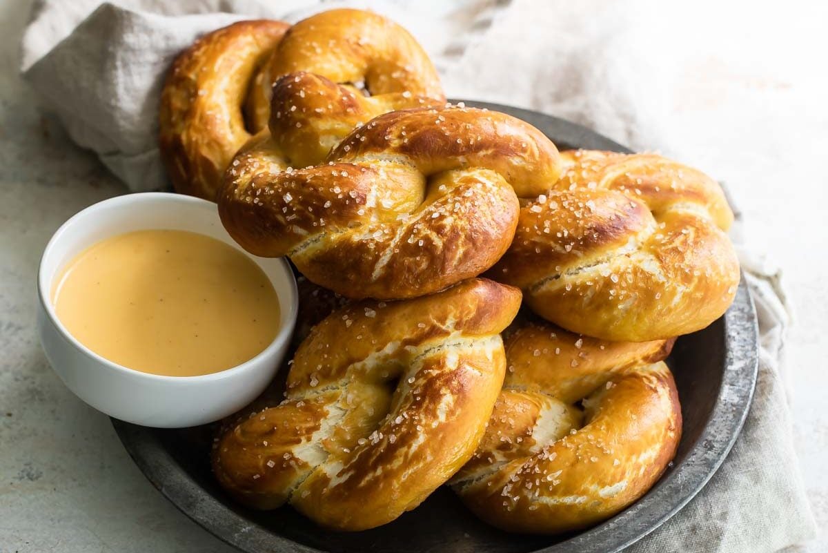 A platter of soft pretzels with a bowl of cheese sauce.