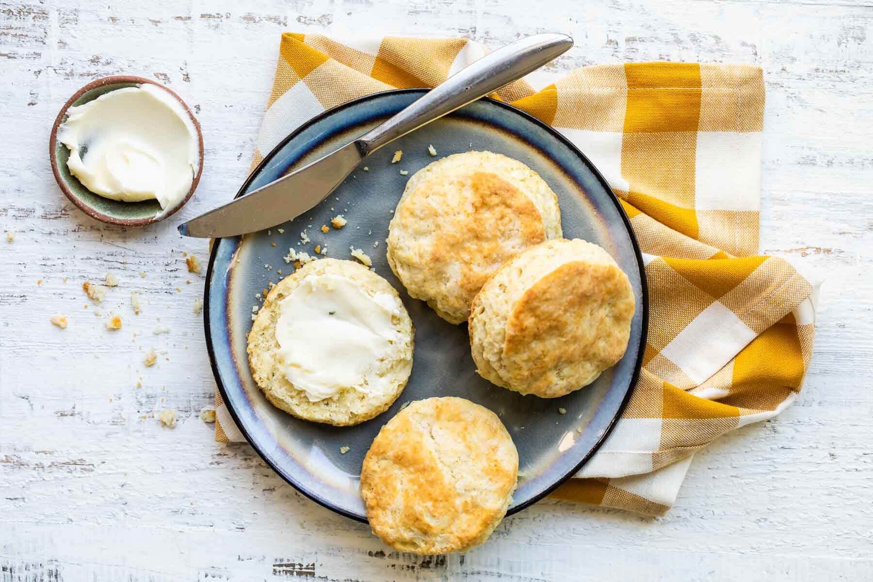 A plate with biscuits cut in half, one piece slathered in butter.