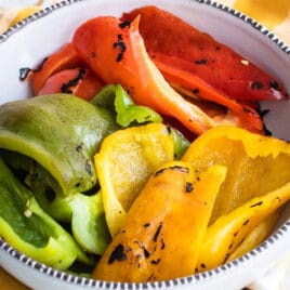 Red, green, and yellow roasted peppers in a bowl.