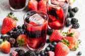 3 glasses and a pitcher of iced tea berry sangria surrounded by piles of fresh berries.