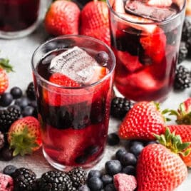 3 glasses and a pitcher of iced tea berry sangria surrounded by piles of fresh berries.