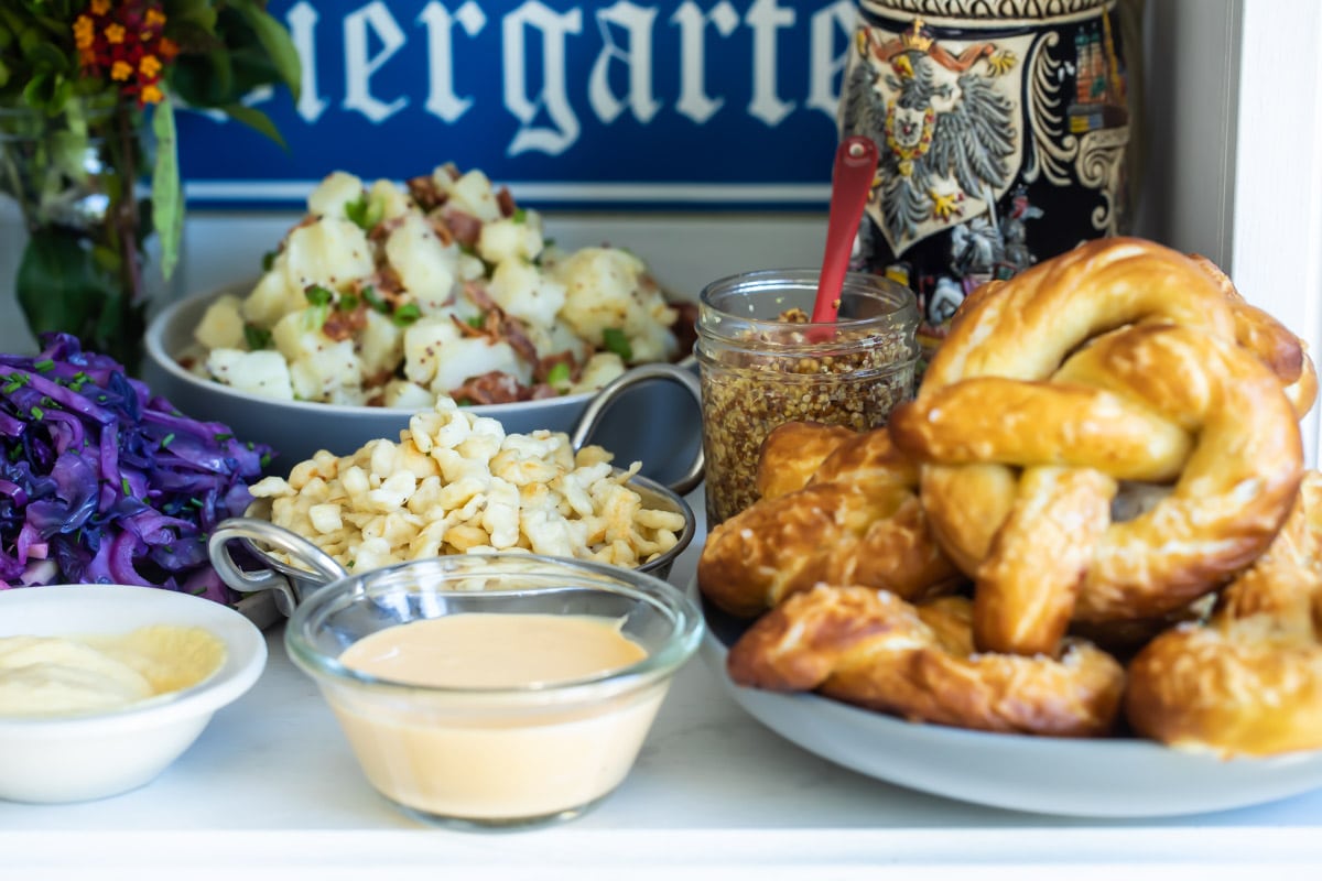 A table of Oktoberfest food including schnitzel, spaetzle, soft pretzels, German potato salad, Lebkuchen, and beer.