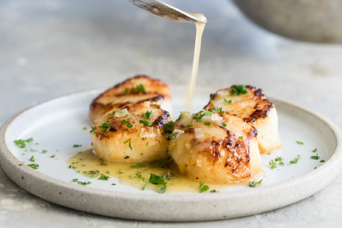 Lemon butter sauce being drizzled onto pan-seared scallops.