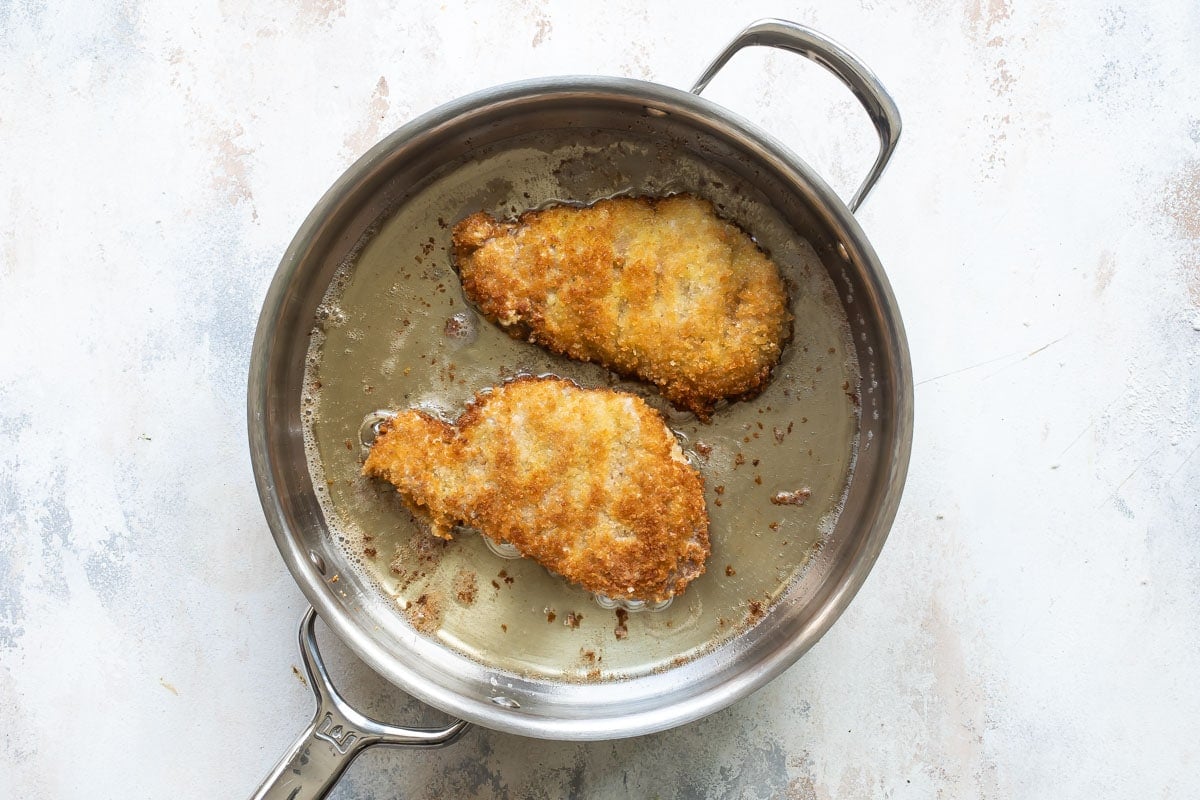Pork schnitzel frying in a pan.