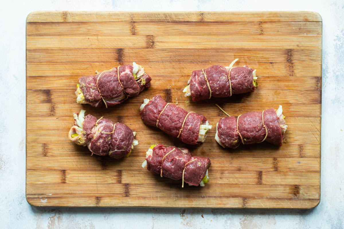 Uncooked rouladen tied on a cutting board.