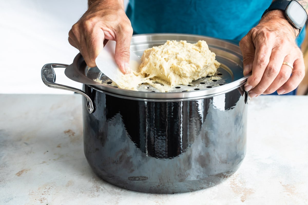 Pushing spaetzle dough through a metal lid with holes to make the dumplings.