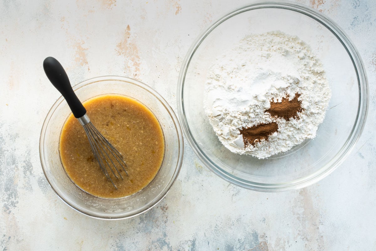 A brown liquid mixture in a clear bowl next to a clear bowl of dry ingredients.