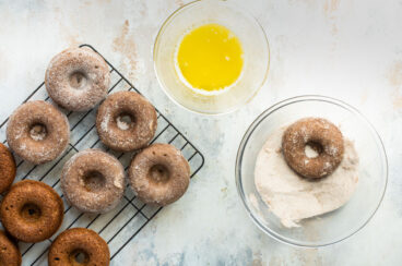 A brown donut being dipped in a cinnamon sugar mixture.