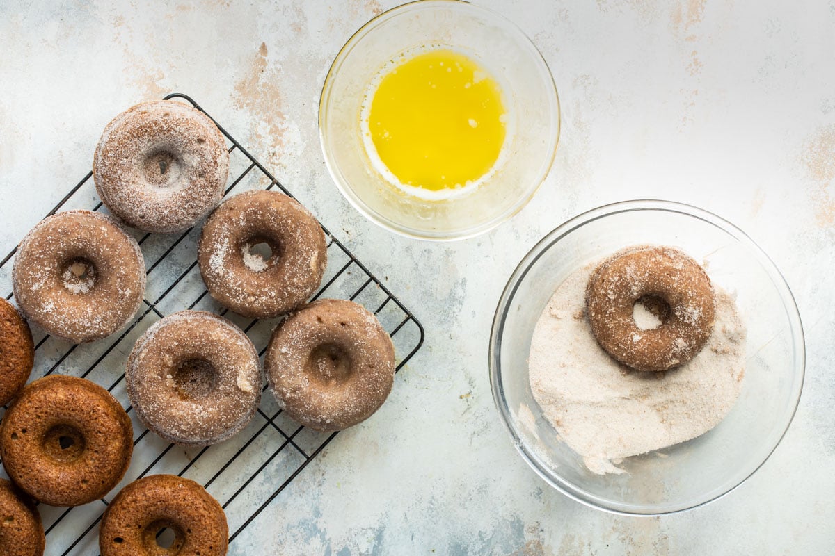 A brown donut being dipped in a cinnamon sugar mixture.