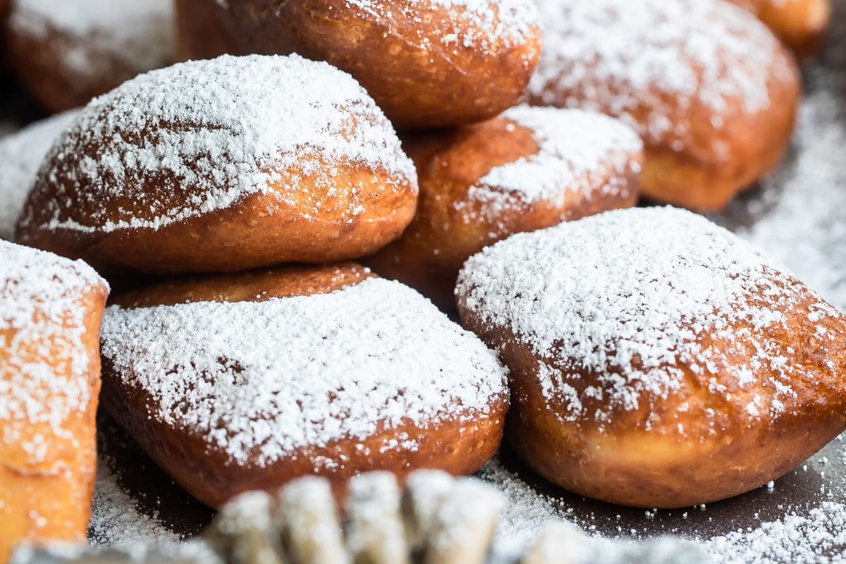 Beignets on a serving platter with powdered sugar sprinkled on top.