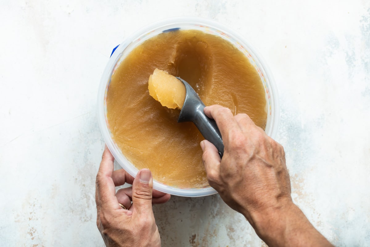 Someone scooping brandy apple cider slush out of an ice cream pail.