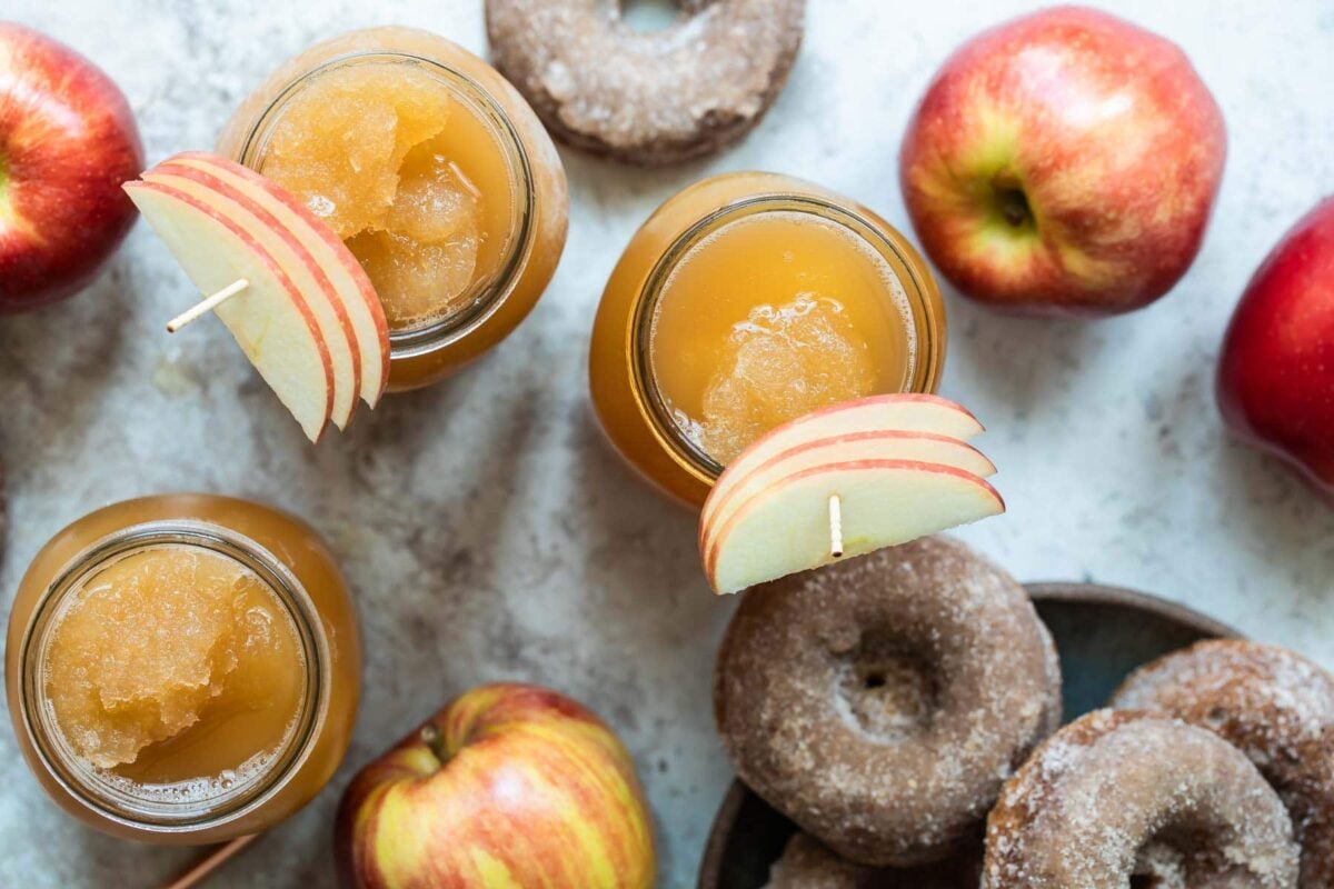 Three mason jars of brandy apple cider slush surrounded by donuts and apples.