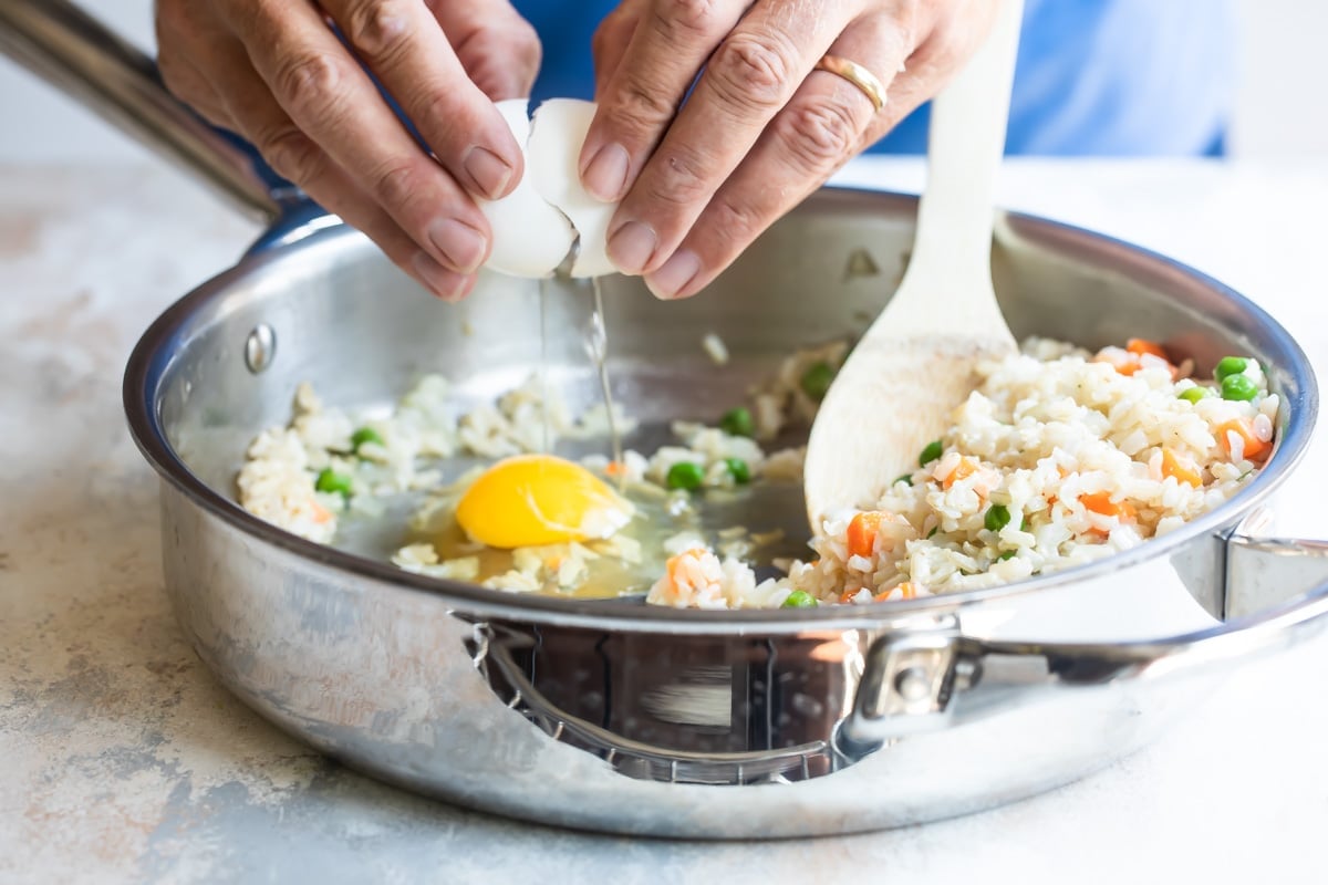 Someone cracking an egg into a fried brown rice mixture.