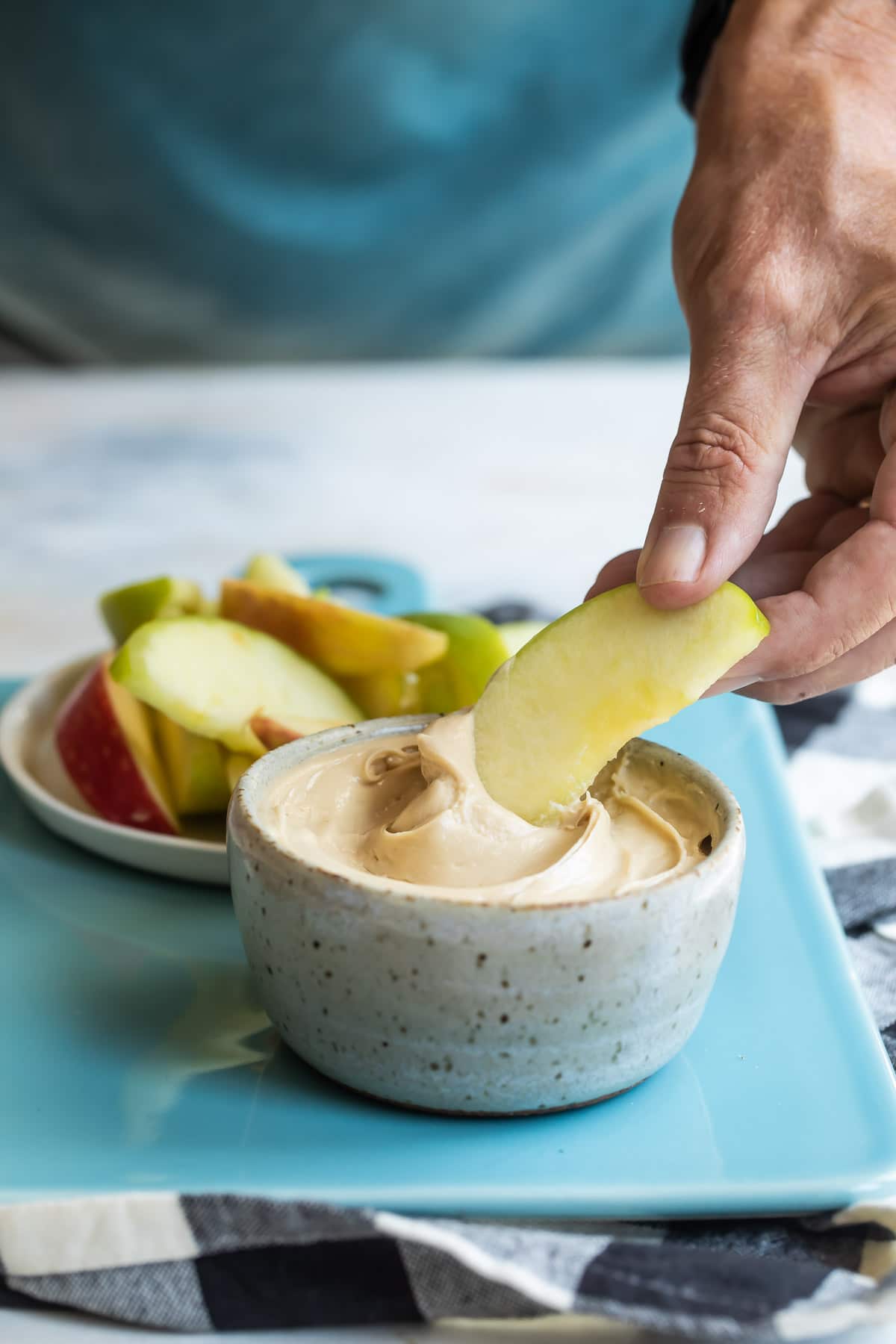 Someone dipping an apple slice into caramel apple dip.