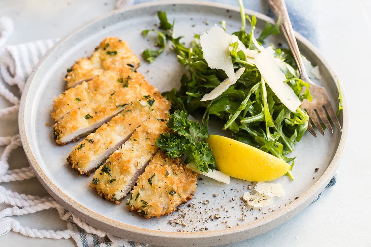 Chicken Milanese on a gray plate with a side of greens.